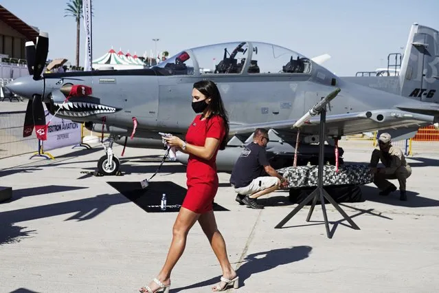 A woman walks past a Beechcraft AT-6 Wolverine light-attack aircraft as crew install a device to its wing at the Dubai Air Show in Dubai, United Arab Emirates, Sunday, November 14, 2021. The biennial Dubai Air Show opened Sunday as commercial aviation tries to shake off the coronavirus pandemic. (Photo by Jon Gambrell/AP Photo)
