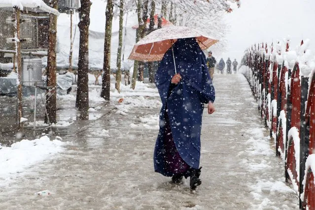 An Afghan burqa-clad woman carrying an umbrella walks along a pavement during snowfall in Fayzabad, Badakhshan province on February 19, 2024. (Photo by Omer Abrar/AFP Photo)