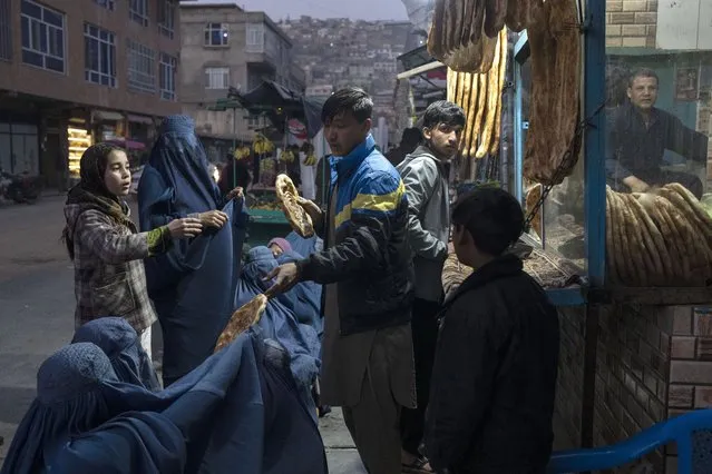 A man distributes bread to Burka-wearing Afghan women outside a bakery in Kabul, Afghanistan, Thursday, December 2, 2021. According to U.N. figures from early November, almost 24 million people in Afghanistan, around 60% percent of the population, suffer from acute hunger, including 8.7 million living in near famine. Increasing numbers of malnourished children have filled hospital wards. (Photo by Petros Giannakouris/AP Photo)