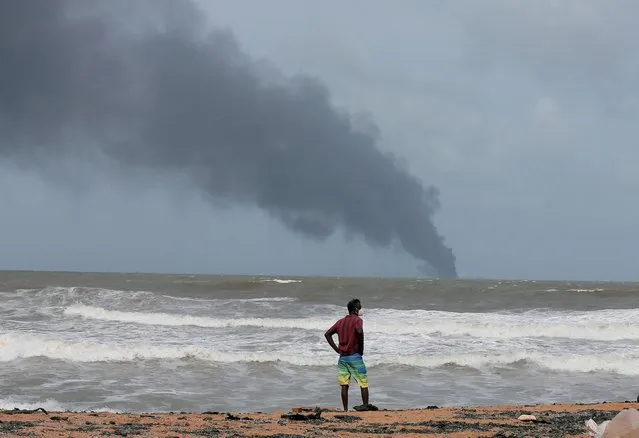 A man wearing a protective mask looks on as smoke rises from a fire onboard the MV X-Press Pearl container ship in the seas off the Colombo Harbour in Ja-Ela, Sri Lanka on May 26, 2021. The vessel, sailing with a Singaporean flag and carrying cosmetics and chemicals including 25 tonnes of nitric acid, was anchored off the Colombo harbour when a container caught fire. (Photo by Dinuka Liyanawatte/Reuters)
