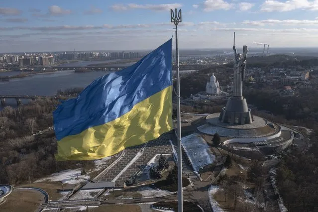 A view of Ukraine's national flag waves above the capital with the Motherland Monument on the right, in Kyiv Sunday, February 13, 2022. Some airlines have halted or diverted flights to Ukraine amid heightened fears that an invasion by Russia is imminent despite intensive weekend talks between the Kremlin and the West. (Photo by Efrem Lukatsky/AP Photo)