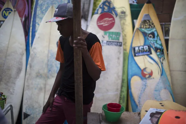 Robert Silva watches as boards are repaired at the Rocinha Surf Association headquarters in the Rocinha slum in Rio de Janeiro, Brazil, Thursday, July 2, 2015. Along with free surf boards and clothes, kids are taught how to maintain and fix their gear. (Photo by Felipe Dana/AP Photo)