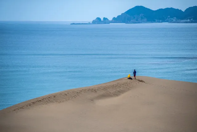 People visit Tottori Sand Dunes on August 27, 2019 in Tottori, Japan. The Tottori Sand Dunes form the only large dune system in Japan and were created by sediment deposits carried by the Sendai River into the Sea of Japan. Sea currents and wind brought the sand from the sea floor to the shore, where the wind constantly rearranges the shape. The dunes have existed for over 100,000 years but are now decreasing due to a post-war government reforestation program and concrete barriers erected to protect the coast from tsunamis which have disrupted the currents responsible for bringing the sand to shore. Although authorities have begun measures to protect the dunes, including dumping sand off the shore in the hope that it will wash ashore, as well as employing the manual removal of encroaching grassy areas, the result is as yet unclear. (Photo by Carl Court/Getty Images)