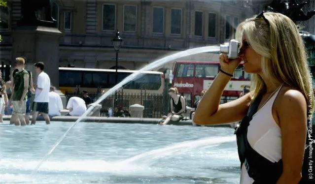 A tourist takes a photograph near a  fountain in Trafalgar Square