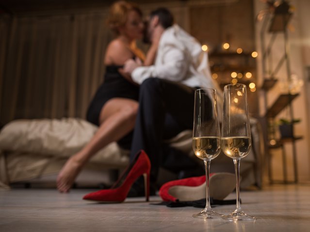 Focus on two glasses of champagne on floor. Ardent loving couple is sitting on bed and hugging with passion on background. Romantic date concept. (Photo by Olena Yakobchuk/Rex Features/Shutterstock)