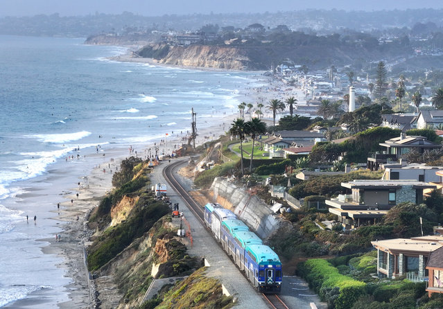 An aerial view of a Coaster commuter train passing along eroding cliffs at the Pacific Ocean coastline on August 16, 2024 in Del Mar, California. Rising sea levels and stronger storms have contributed to increased erosion and landslides along the vital Amtrak Pacific Surfliner coastal rail corridor which runs over 350 miles through Southern California to California’s Central Coast. Erosion and landslides on coastal bluffs led to three extended closures along the route in 2023 and 2024 and twelve shutdowns in the past six years. With climate change expected to bring more intense storms and higher seas, most officials believe vulnerable sections of the corridor will need to be moved inland. The scenic route is the second-most popular Amtrak corridor in the country and also serves commuter and freight trains. (Photo by Mario Tama/Getty Images)