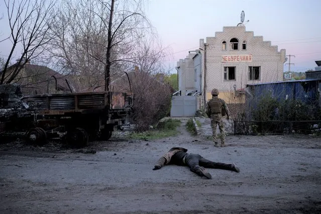 A Ukrainian serviceman stands next to the body of a suspected Russian soldier, in the village of Vilkhivka, recently retaken by Ukraininan forces near Kharkiv, Ukraine, Monday, May 9, 2022. (Photo by Felipe Dana/AP Photo)