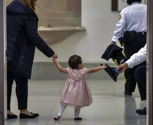 Kimberly Del Cid, 1, center, reaches for the hat of Officer Edward Twine while waiting for her father, Mauricio Del Cid, to be sworn in as a new U.S. citizen in front of the original Declaration of Independence, the Constitution and the Bill of Rights, in the Rotunda of the National Archives in Washington on December 16, 2019. (Photo by Bill O’Leary/The Washington Post)