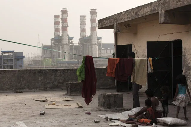 A family sits next to a washing line on the roof of a building as chimneys the 1500 Megawatt Combined Cycle Power Station Bawana operated by Pragati Power Corp. (PPCL) stand in the distance in Bawana, Delhi, India on Tuesday, May 3, 2016. About 25 kilometers (16 miles) northwest of Prime Minister Narendra Modi's office in New Delhi, a $780 million gas-fired electricity plant that could reduce the choking pollution in India's capital is operating at a fraction of its potential. The facility ran at about a sixth of capacity on Monday, while a much older, belching coal plant some 15 kilometers southeast of central New Delhi provided the biggest share of the city's power generation. (Photo by Udit Kulshrestha/Bloomberg)