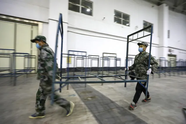 Soldiers build beds in a convention center that has been converted into a temporary hospital in Wuhan in central China's Hubei Province, Tuesday, February 4, 2020. China said Tuesday the number of infections from a new virus surpassed 20,000 as medical workers and patients arrived at a new hospital and President Xi Jinping said “we have launched a people's war of prevention of the epidemic”. (Photo by Chinatopix via AP Photo)