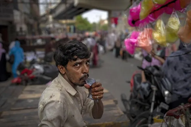 A roadside cotton candy vendor drinks water from a plastic pouch as he waits for customers at a weekly market in New Delhi, India, Wednesday, June 29, 2022. (Photo by Altaf Qadri/AP Photo)