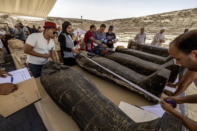 Archaeologists measure the length to register one of the sarcophaguses found in a cache dating to the Egyptian Late Period (around the fifth century BC), discovered by a mission headed by Egypt's Supreme Council of Antiquities, at the Bubastian cemetery at the Saqqara necropolis, southwest of Egypt's capital on May 30, 2022. - Egypt on May 30 unveiled a cache of 150 bronze statues depicting various gods and goddesses including “Bastet, Anubis, Osiris, Amunmeen, Isis, Nefertum and Hathor”, along with 250 sarcophagi at the Saqqara archaeological site south of Cairo, the latest in a series of discoveries in the area. (Photo by Khaled Desouki/AFP Photo)