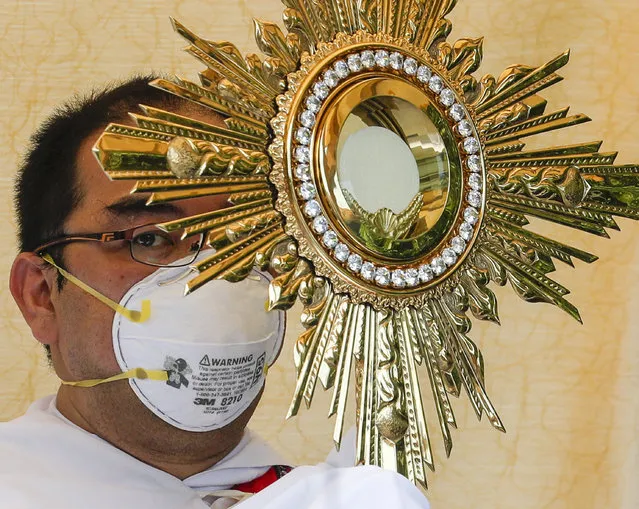 A Catholic priest wearing a protective mask holds a Monstrance with the Sacred Host as he rides a pick-up truck around villages during a new Palm Sunday ritual to help prevent the spread of the new coronavirus in Manila, Philippines on Sunday, April 5, 2020. Catholic devotees usually troop to churches on Palm Sunday to have their palm fronds blessed to commemorate the entry of Jesus Christ into Jerusalem. (Photo by Aaron Favila/AP Photo)