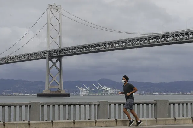 A man wears a mask to protect himself from the coronavirus while running in front of the San Francisco-Oakland Bay Bridge along the Embarcadero in San Francisco, Sunday, April 5, 2020. (Photo by Jeff Chiu/AP Photo)