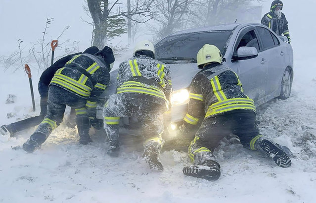 In this photo provided by the Ukrainian Emergency Service, Ukrainian Emergency workers try to push a car trapped in snow on the Odesa region highway, Ukraine, Monday, November 27, 2023. Heavy snowfalls and storm has hit Ukraine on Monday leaving more than 2,000 towns and villages in war-torn country without power. (Photo by Ukrainian Emergency Service via AP Photo)