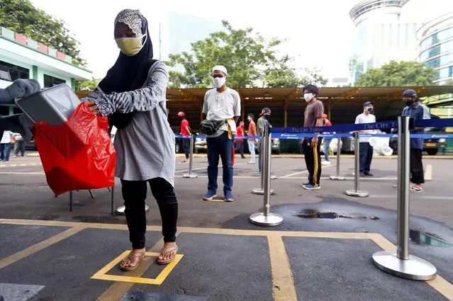 People wearing protective face masks practice social distancing while receiving rice from an automated rice ATM distributor amid the spread of the coronavirus disease (COVID-19) in Jakarta, Indonesia on May 4, 2020. (Photo by Ajeng Dinar Ulfiana/Reuters)