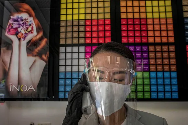 A receptionist with a protective mask and a face shield answers a call at a hair salon in Bangkok, Thailand, Tuesday, May 5, 2020. Residents of the Thai capital Bangkok strolled in its parks, booked haircuts and stocked up on beer and other alcoholic drinks as Thai government eased restrictions on May 3 that were imposed weeks ago to combat the spread of COVID-19. (Photo by Gemunu Amarasinghe/AP Photo)