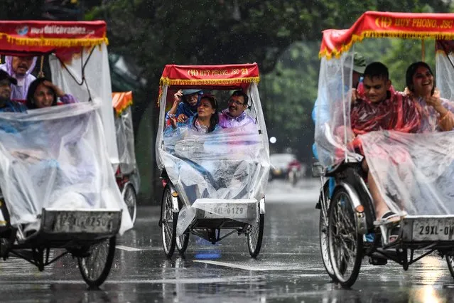 Tourists take a city tour on a cyclo during rainfall, in downtown Hanoi, on August 12, 2022. (Photo by Nhac Nguyen/AFP Photo)