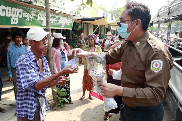 A Red Cross member distributes a face mask to a man to help stop the spread of the new coronavirus at a local market Sunday, April 12, 2020, in Myttha, Myanmar. (Photo by Aung Shine Oo/AP Photo)