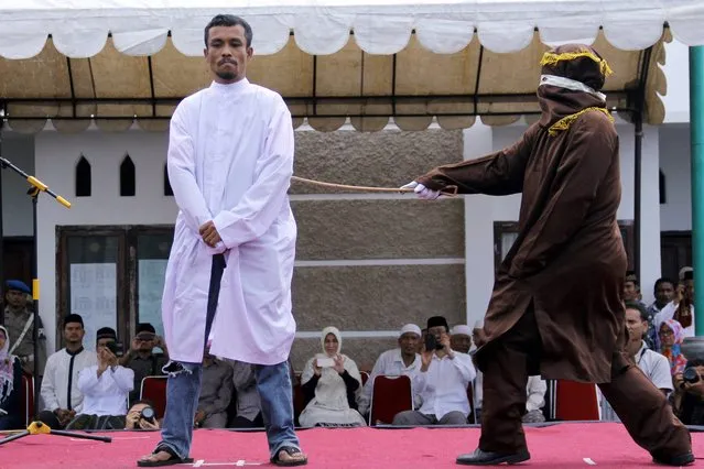 An Islamic Shariah law official whips a man, convicted of gambling, with a rattan cane watched by people inside a mosque compound in Banda Aceh, Aceh Province, Indonesia, Friday, October 3, 2014. Indonesian authorities publicly caned four men who were convicted of gambling in conservative Aceh province after Friday prayers. (Photo by Heri Juanda/AP Photo)