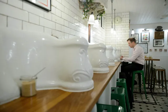 A man sits on the counter with original urinals in “Attendant”, a former public toilet that has been converted into a coffee shop and sandwich bar in central London, on October 3, 2014. With spiralling land prices turning even the darkest corners of London into potential goldmines, the city's forgotten spaces, including 19th-century public toilets, are blossoming into restaurants, cafes and boutiques. (Photo by Leon Neal/AFP Photo)
