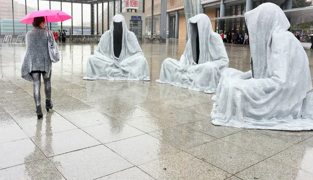 A woman walks past the installation “Waechter der Zeit” (lit. guardians of time) at Potsdamer Platz in Berlin, Germany, October 16, 2014. The three sculptures are on display as part of the “Festival of Lights” until Ocotober 19. (Photo by Stephanie Pilick/EPA)