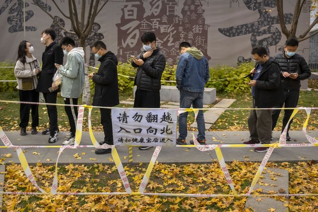 People wearing face masks stand in line for COVID-19 tests at a coronavirus testing site in Beijing, Saturday, November 19, 2022. Performances have been suspended at one of Beijing's oldest and most renowned theaters amid a new wave of shop and restaurant closures in response to a spike in COVID-19 cases in the Chinese capital. (Photo by Mark Schiefelbein/AP Photo)