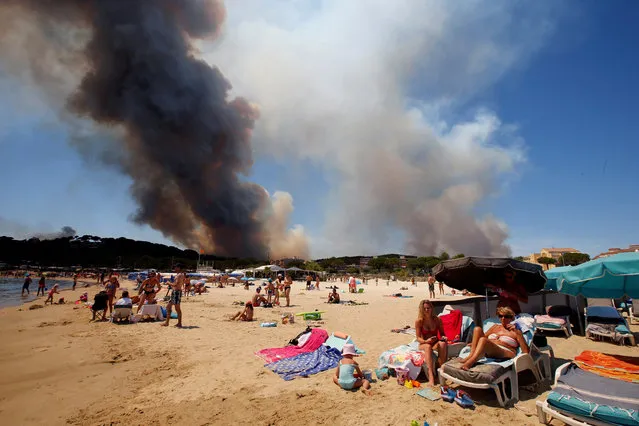 Smoke fills the sky above a burning hillside as tourists relax on the beach in Bormes-les-Mimosas, in the Var department, France, July 26, 2017. (Photo by Jean-Paul Pelissier/Reuters)