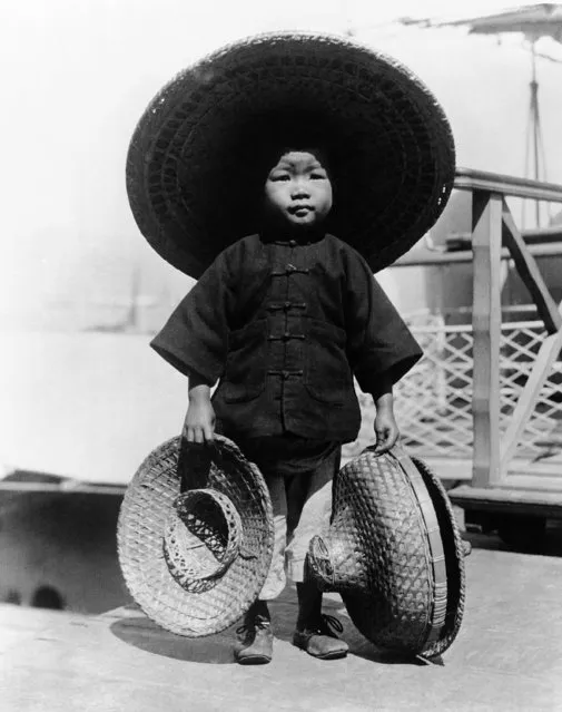 An unhappy looking Chinese boy sheltering from the intense heat of the midday sun and holding smaller hats around December 9, 1930. (Photo by AP Photo)
