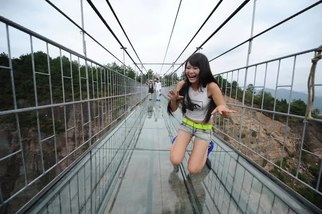 A visitor kneels on the 180-meter-high and 300 meter-long glass-bottomed suspension bridge at the Shiniuzhai National Geopark in Pingjiang county, in central China's Hunan province, 24 September 2015. Tourists visited a glass-bottomed suspension bridge that sits 180 metres above the ground at the Shiniuzhai National Geopark in Pingjiang county, in central China's Hunan province on Thursday (24 September 2015). The 300 metre-long suspended bridge, which apparently sways in the wind, spans a chasm at the national park, popular with tourists for its unique rock formations and geography. Walkers see clear, stomach-churning views of the ground 180 metres below. Park management authorities added a small section of glass last year but decided to transform the entire length of the crossing. The floor is made of a double layer of glass and is 24mm thick in total. (Photo by Jiao Zi/Imaginechina)