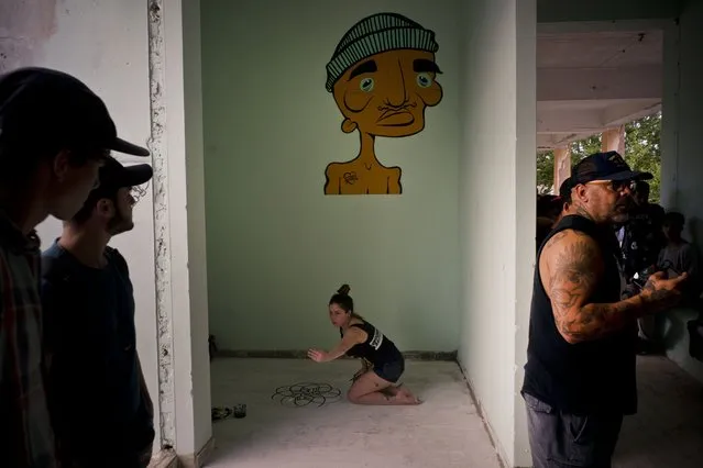 In this January 11, 2018 photo, an artist decorates the floor with a mural during the inauguration of a new recreational space for skateboarders, created in an abandoned gym at the Educational complex Ciudad Libertad, a former military barracks that the late Fidel Castro turned into a school complex after the revolution in Havana, Cuba. The mural on the wall is by Kaya, the late son of Rene Lecour, who stands at right, who founded the skating association “Amigo Skate Cuba” with his skate enthusiast son who wanted to find a way to support Cuba's emerging skater community. (Photo by Ramon Espinosa/AP Photo)