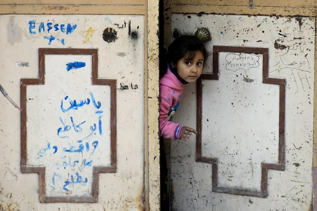 A girl peers through a door in Syria's devastated city of Raqa on January 9, 2018. (Photo by Delil Souleiman/AFP Photo)