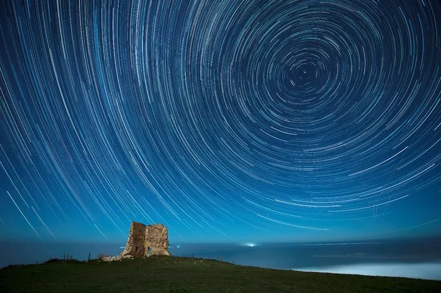 An overlay image of 128 photographs shows circumpolar star trails over San Telmo tower in Ubiarco, Cantabria, Spain, early 14 December 2021, during the Gemenids meteor shower. (Photo by Pedro Punte Hoyos/EPA/EFE)