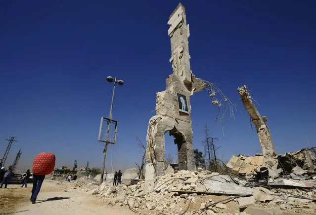 A picture of Syria's President Bashar al-Assad is displayed on a damaged structure at the entrance of al-Dukhaneya neighbourhood near Damascus, as civilians carry their belongings recovered from their homes after soldiers loyal to Syria's President Bashar al-Assad regained control of the area from rebel fighters, in this October 7, 2014 file photo. (Photo by Omar Sanadiki/Reuters)