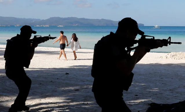 Tourists walk past a SWAT police team during a military and police drill in preparation for the temporary closure of the holiday island Boracay in Philippines April 24, 2018. (Photo by Erik De Castro/Reuters)