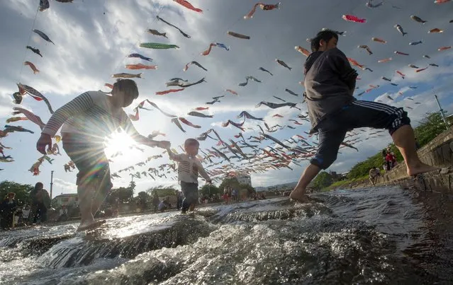 Japanese father's and sons cross a stream below a group of one thousand large carp kites flown in the air during Golden Week in Takatsuki city, Osaka prefecture, Japan, 03 May 2018. The carp kites, which symbolize strength, energy and courage are flown from late April until May 5th, or Children's Day in Japan. Children's Day is one of the holidays during Golden Week, a series of annual holidays in Japan at the beginning of May. (Photo by Everett Kennedy Brown/EPA/EFE/Rex Features/Shutterstock)