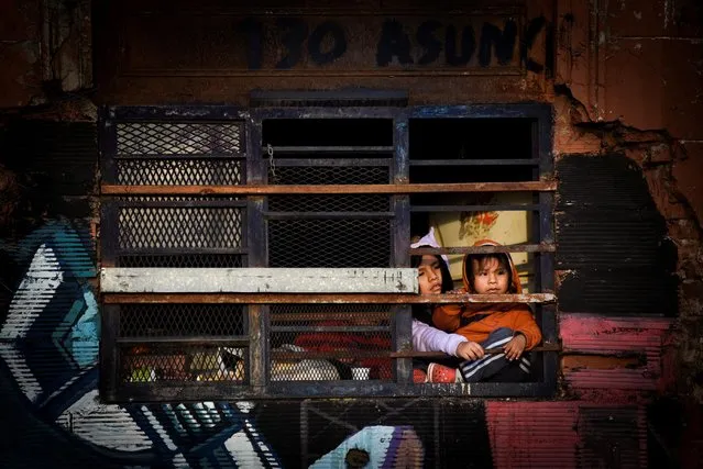 Children look through a fenced window as unemployed and informal workers protest to demand more subsidies from the national government, in Buenos Aires, Argentina on April 19, 2023. (Photo by Mariana Nedelcu/Reuters)