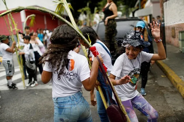 Junior members of the Palmeros de Chacao brotherhood get wet with a hose while carrying packs of palm leaves to be blessed at a Catholic church to mark the beginning of the Holy Week, in Caracas, Venezuela on April 1, 2023. (Photo by Leonardo Fernandez Viloria/Reuters)