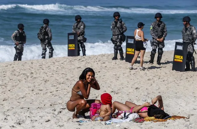 Women relax near National Force soldiers on Barra da Tijuca beach in front of Hotel Windsor, where the auction for Libra offshore oilfield will take place, in Rio de Janeiro, on Oktober 21, 2013. Brazil geared up on Monday to sell production rights to Libra, its largest-ever oil discovery, in a landmark auction that sparked widespread nationalist protests even though most of the world's premier energy companies opted to stay away. (Photo by Sergio Moraes/Reuters)