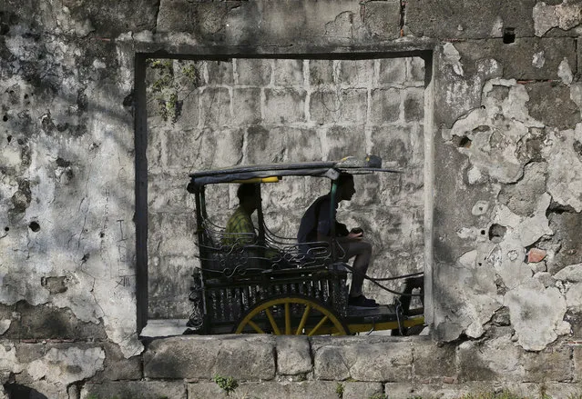 A tourist, right, rides a horse-drawn carriage locally known as “Kalesa” around the historic walled city of Intramuros in Manila, Philippines on Monday, March 16, 2015. The tour costs P350 (about US$8) per passenger. (Photo by Aaron Favila/AP Photo)