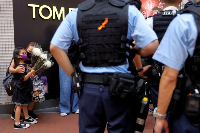 A mother and child holding flowers are stopped and searched by police as they try to pay tribute to a man, who stabbed a policeman then stabbed himself in the chest with the knife and died on the anniversary of the city's return to Chinese rule, at Causeway Bay in Hong Kong, China on July 2, 2021. (Photo by Tyrone Siu/Reuters)