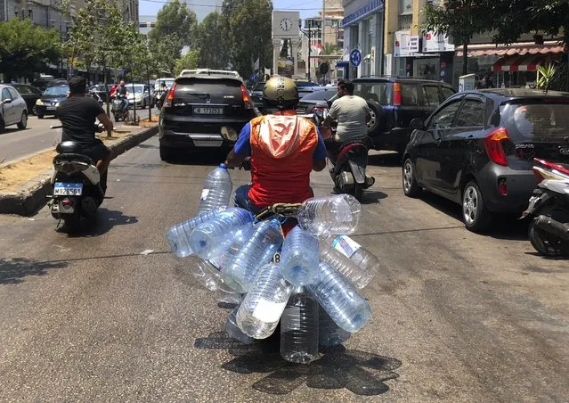 A man rides his scooter with empty water bottles to fill them with gasoline, in Beirut, Lebanon, Wednesday, June 23, 2021. Lebanon is struggling amid a 20-month-old economic and financial crisis that has led to shortages of fuel and basic goods like baby formula, medicine and spare parts. The crisis is rooted in decades of corruption and mismanagement by a post-civil war political class. (Photo by Hussein Malla/AP Photo)
