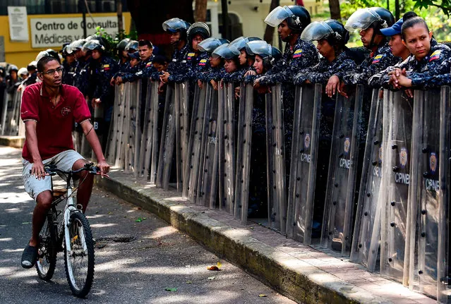 A man rides his bicycle as policemen stand on the sidewalk before a demonstration called by union leaders to demand labour protection against dismissals of civil servants in Caracas on March 19, 2019. The demonstration was finally called off due to the large deployment of security forces in the streets. (Photo by Ronaldo Schemidt/AFP Photo)