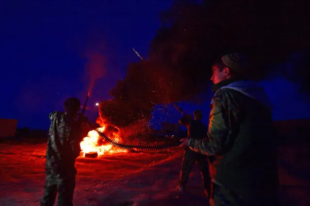 A fighter with the Kurdish-led Syrian Democratic Forces (SDF) fire shots in the air as they stand around a bonfireduring Nowruz (Noruz) celebrations near the village of Baghouz in the countryside of the eastern Syrian province of Deir Ezzor on March 20, 2019, as battles continue to capture the Islamic State (IS) groups last scrap of territory. The Persian New Year is an ancient Zoroastrian tradition celebrated by Iranians and Kurds which coincides with the vernal (spring) equinox and is calculated by the solar calendar. (Photo by Giuseppe Cacace/AFP Photo)