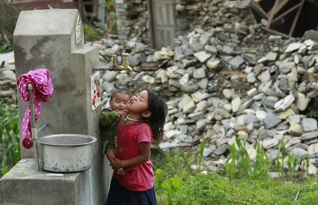 A young girl holding a baby takes a cool drink from a water spigot in the destroyed village of Balua, near the epicenter of Saturday's massive earthquake, in the Gorkha District of Nepal, Thursday, April 30, 2015. (Photo by Wally Santana/AP Photo)