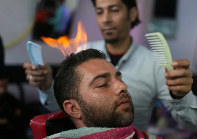 Palestinian barber Ramadan Odwan styles and straightens the hair of a customer with fire at his salon in Rafah, in the southern Gaza Strip February 2, 2017. (Photo by Ibraheem Abu Mustafa/Reuters)
