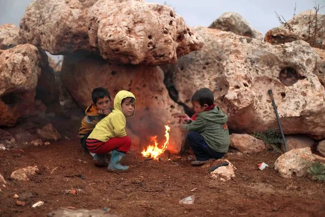 Children on November 20, 2021, gather in front of a camp fire, in the Bardaqli camp for displaced people in the town of Dana in Syria's northwestern Idlib province, as winter approaches on the International Day of Children's Rights. (Photo by Aaref Watad/AFP Photo)