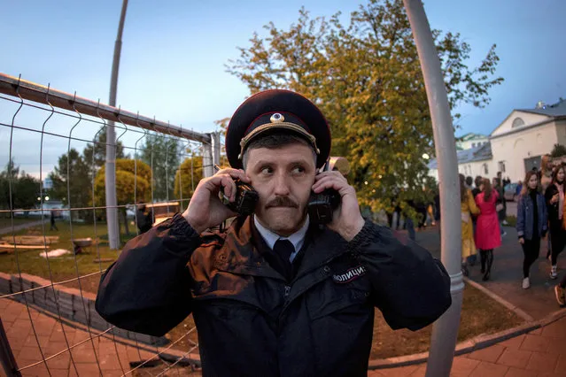 A police officer speaks on two walkie talkies as demonstrators gather in front of a new builded fence blocked by police to protest plans to construct a cathedral in a park in Yekaterinburg, Russia, Wednesday, May 15, 2019. Hundreds of riot police have surrounded a park in Russia's fourth-largest city before what's expected to be a third consecutive day of protests against building a new cathedral. (Photo by Anton Basanayev/AP Photo)