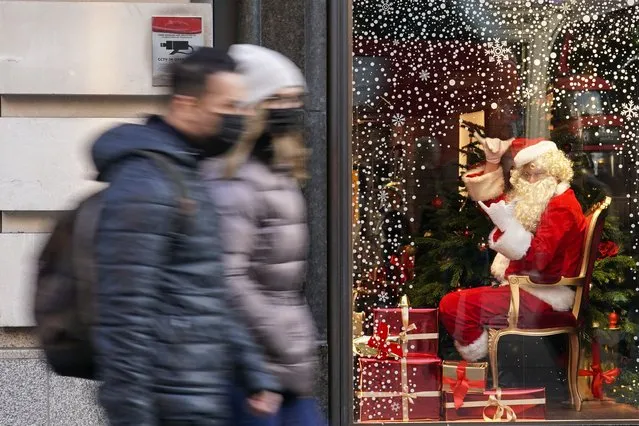 A man dressed as Santa Claus gestures as people walk past, in London, Saturday, December 4, 2021. Britain says it will offer all adults a booster dose of vaccine within two months to bolster the nation's immunity as the new omicron variant of the coronavirus spreads. New measures to combat variant came into force in England on Tuesday, with face coverings again compulsory in shops and on public transport. (Photo by Alberto Pezzali/AP Photo)