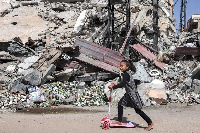 A girl rides a scooter past the rubble of a destroyed building in Rafah in the southern Gaza Strip on April 5, 2024 amid the ongoing conflict in the Palestinian territory between Israel and the militant group Hamas. (Photo by Mohammed Abed/AFP Photo)